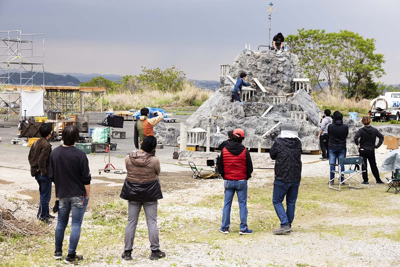 Equipe do Instituto de Pesquisa de Tokusatsu diante de um set com miniatura de rochedo ao ar livre