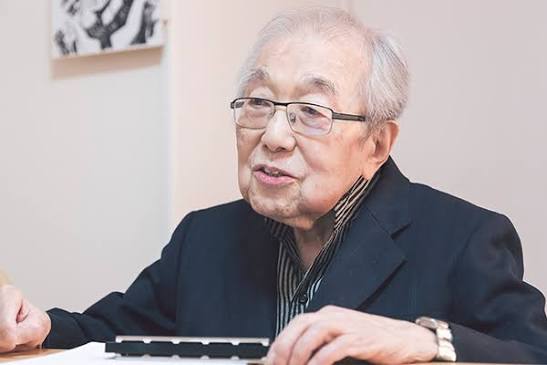 Chumei Watanabe sentado a uma mesa, com um teclado pequeno e anotações à frente