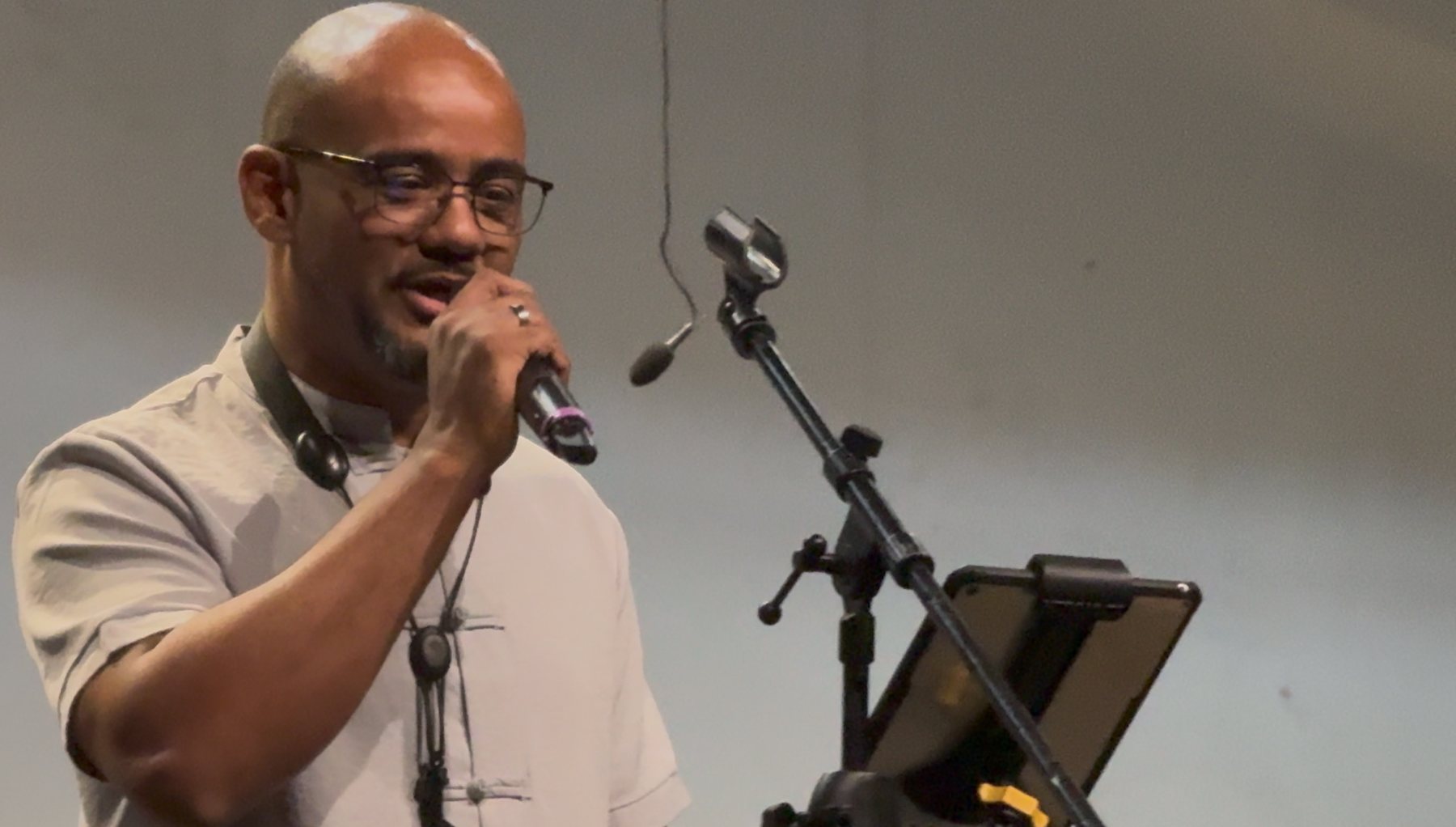 Marcos Andres canta ao microfone, com um tablet de partitura ao lado