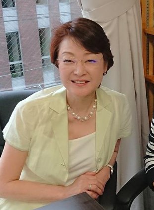 Fukumi Kuroda sorri para a câmera, de óculos, cabelo curto castanho, blazer verde-claro e colar de pérolas