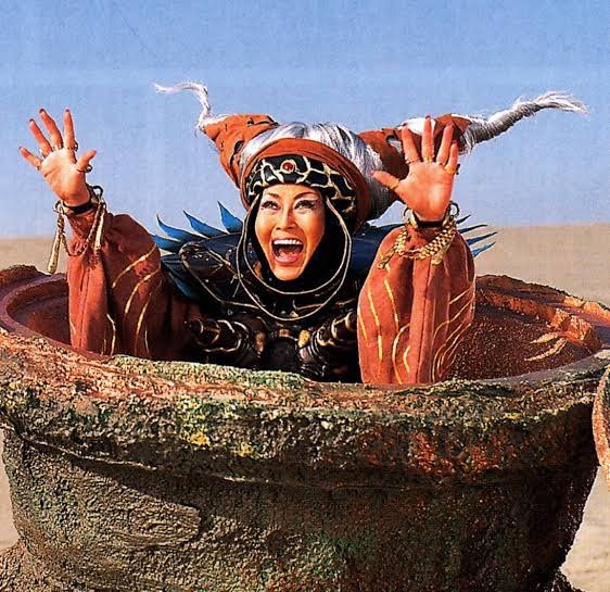 A bruxa Bandora, de braços erguidos e gritando, dentro do caldeirão gigante de Zyuranger