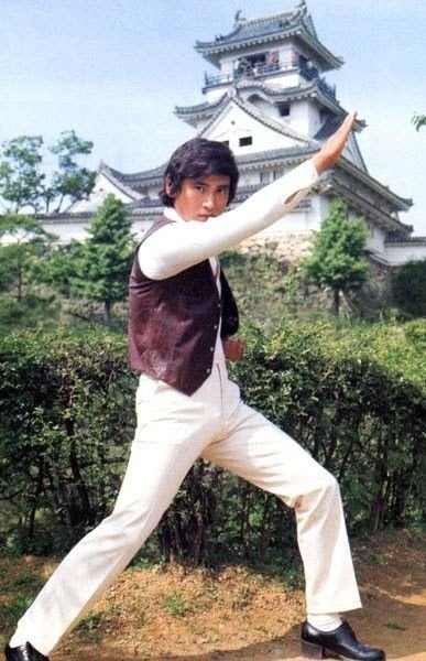 Hiroshi Miyauchi de calça branca e colete, em pose de luta diante de um castelo japonês, nos anos 1970