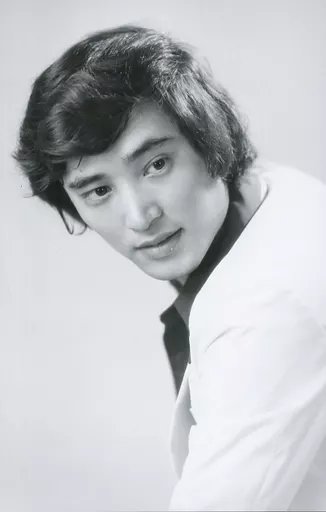 Retrato em preto e branco de Hiroshi Miyauchi jovem, de camisa escura e paletó claro