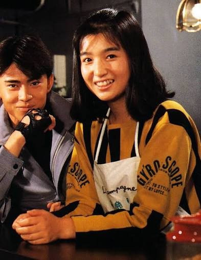 Katsumi Kida, wearing an apron, smiles next to Kotaro Minami at a counter in a Kamen Rider Black still