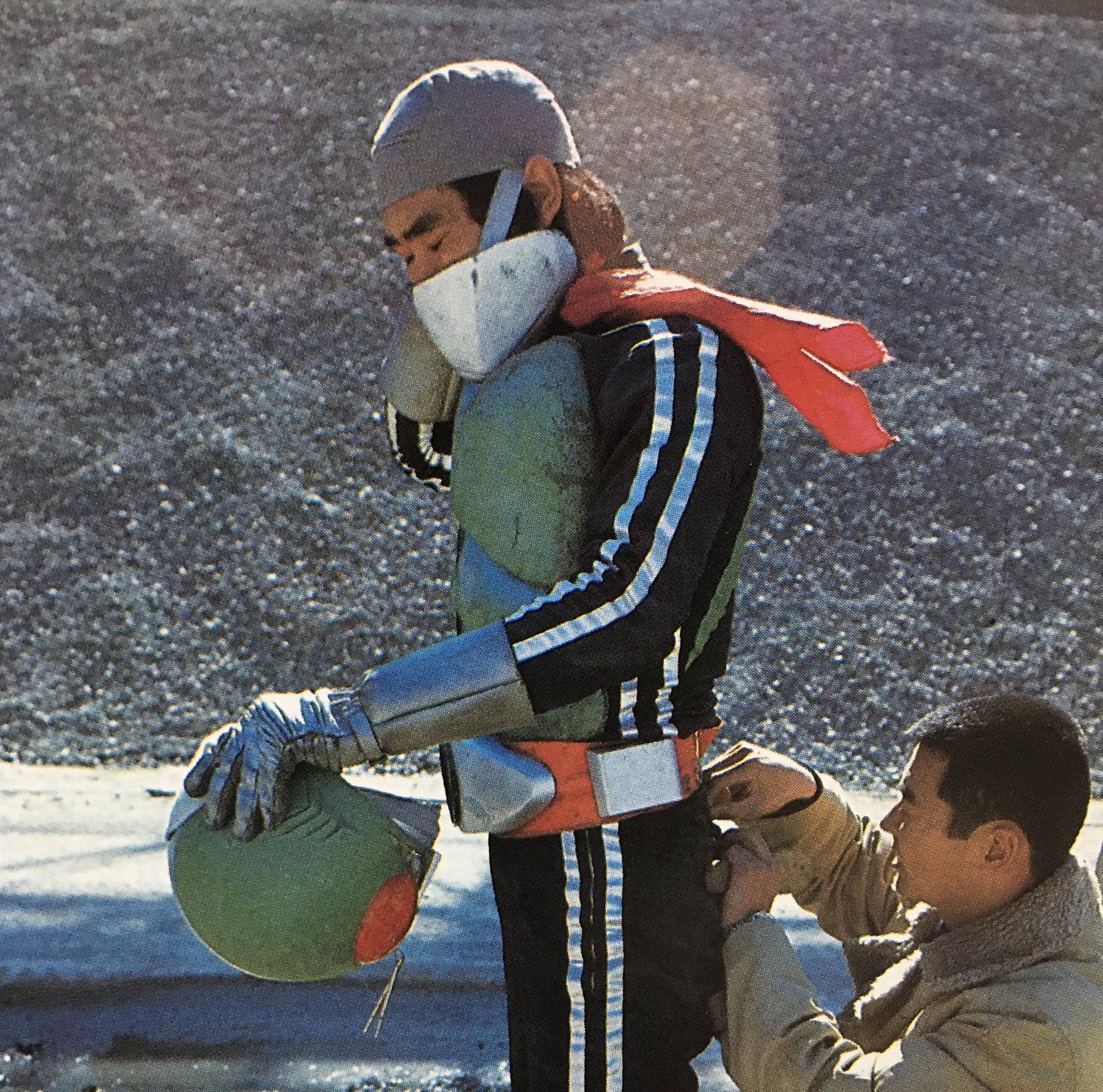 Intérprete de Rider com o traje completo e o capacete na mão, enquanto um integrante da equipe ajusta o cinto