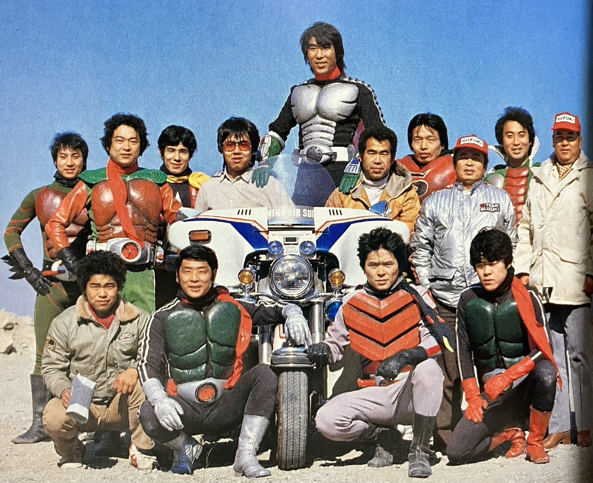 Group of performers in Rider suits from several series around a motorcycle, one standing behind in silver chest armor
