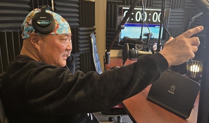 Shocker Ohno in headphones and bandana, pointing upward in a radio studio