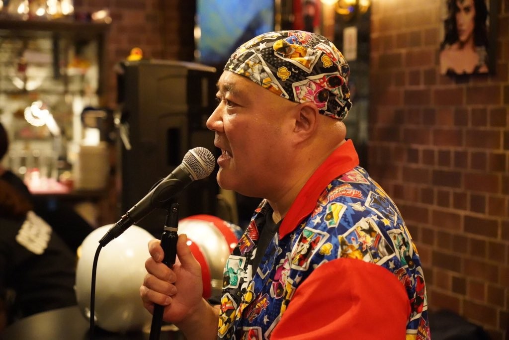Shocker Ohno at the microphone, wearing a bandana printed with Super Sentai heroes