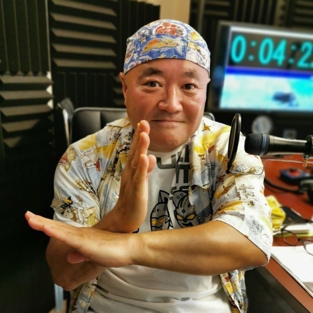 Shocker Ohno in a printed shirt, crossing his arms in a henshin pose in a studio