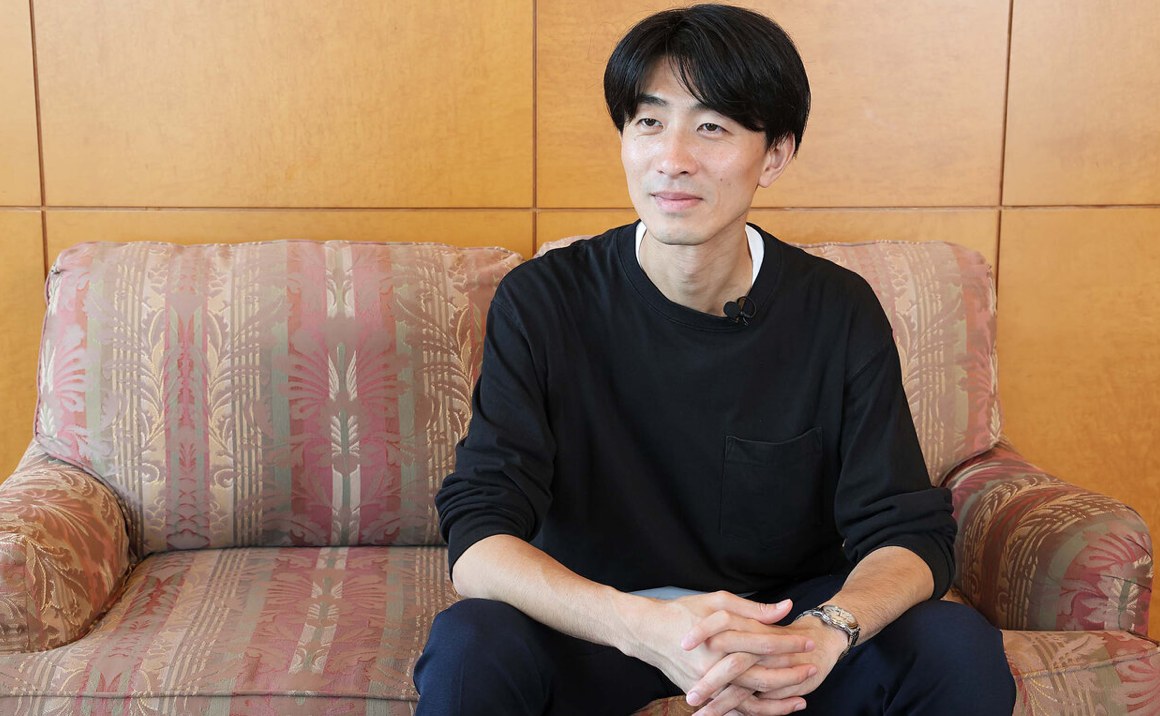 Yoshito Kuji, de camiseta preta, sentado num sofá estampado durante a entrevista ao TELEMAGA.net