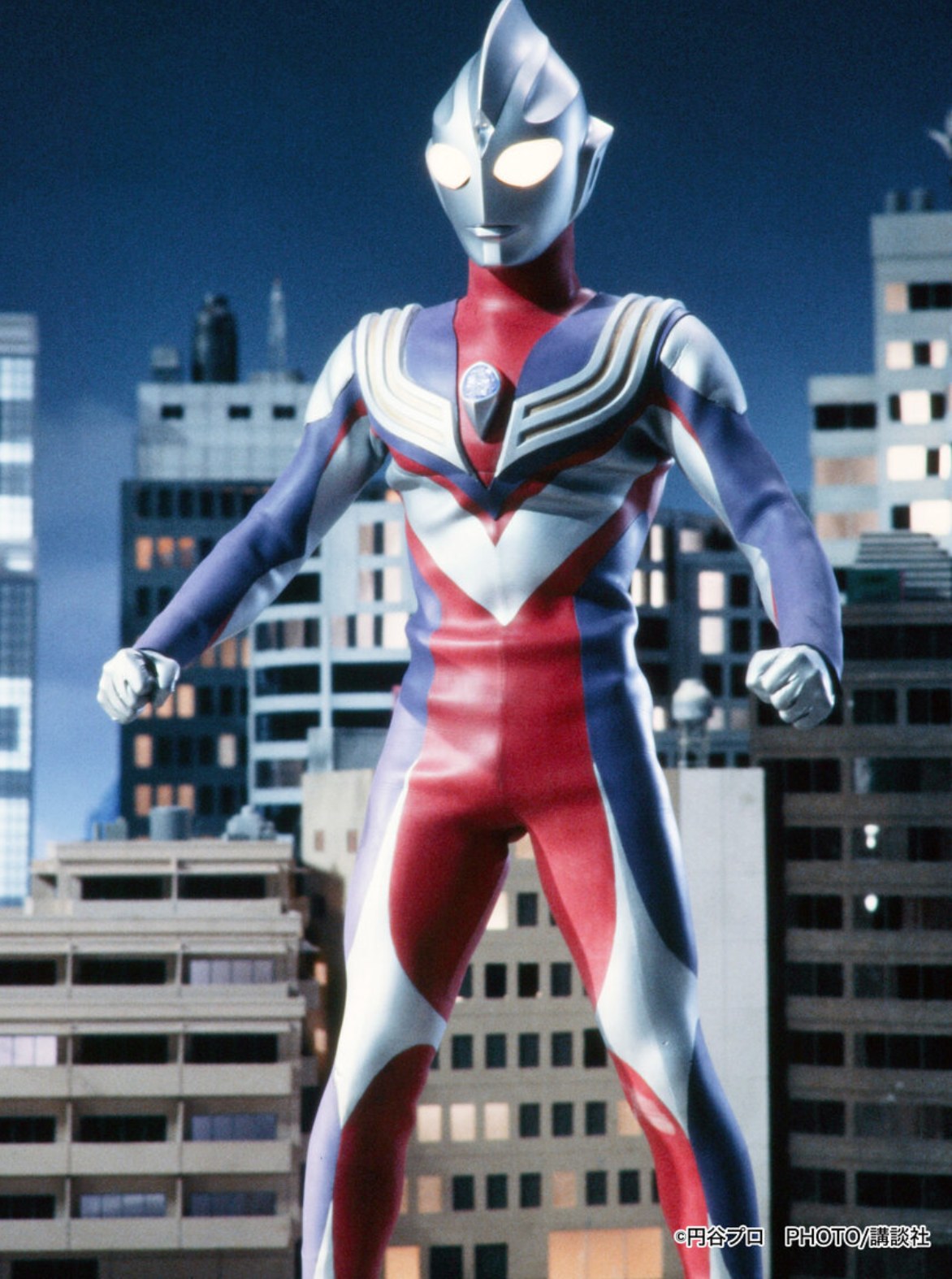 Ultraman Tiga em pose de combate diante dos prédios da cidade